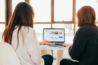 two women talking while looking at laptop computer by KOBU Agency courtesy of Unsplash.